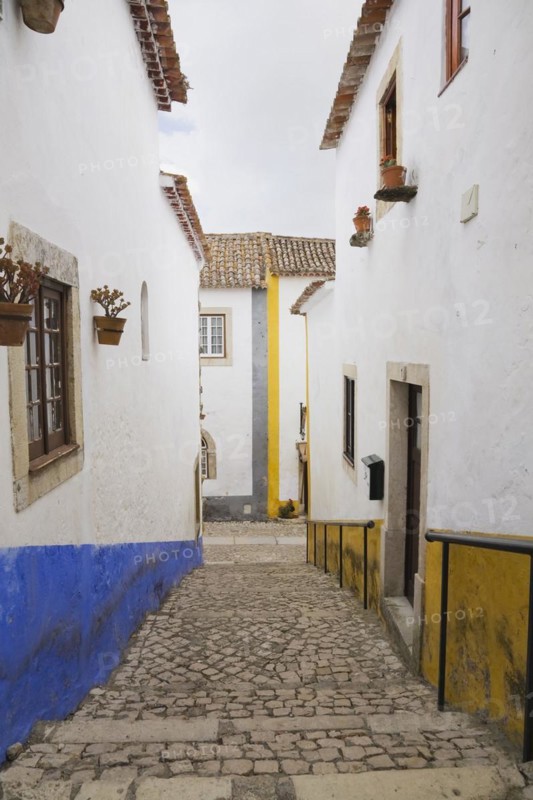 Old street with mosaic style paving stone stairs and white roughcast buildings with blue and yellow painted stripes, Medieval city of Obidos, Portugal, Europe