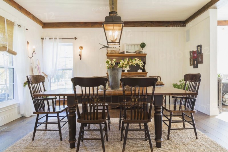 Brown stained pine wood antique reproduction style dining table with high back chairs in dining room with rug and dark brown larch wood floorboards inside country style home, Quebec, Canada, North America