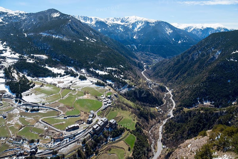 Bergtal mit einem Fluss, grünen und verschneiten Flächen und einer Straße, die sich durch das Tal zieht. Klare Aussicht auf die umliegende Berglandschaft, Mirador del Roc del Quer, Blick auf Canillo, Fürstentum Andorra, Pyrenäen