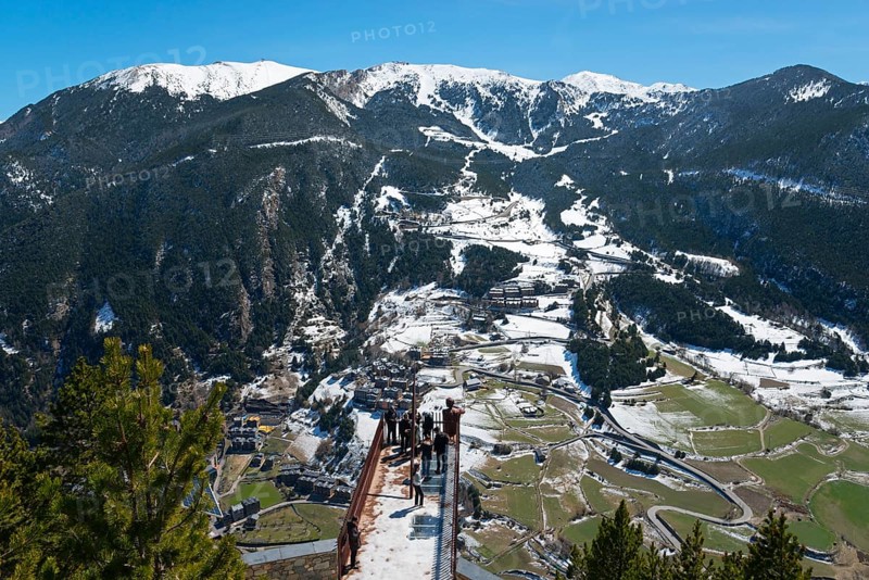 Mehrere Menschen stehen auf einem Aussichtspunkt und genießen die schneebedeckte Berglandschaft und das darunter liegende Tal, Mirador del Roc del Quer, Blick auf Canillo, Fürstentum Andorra, Pyrenäen