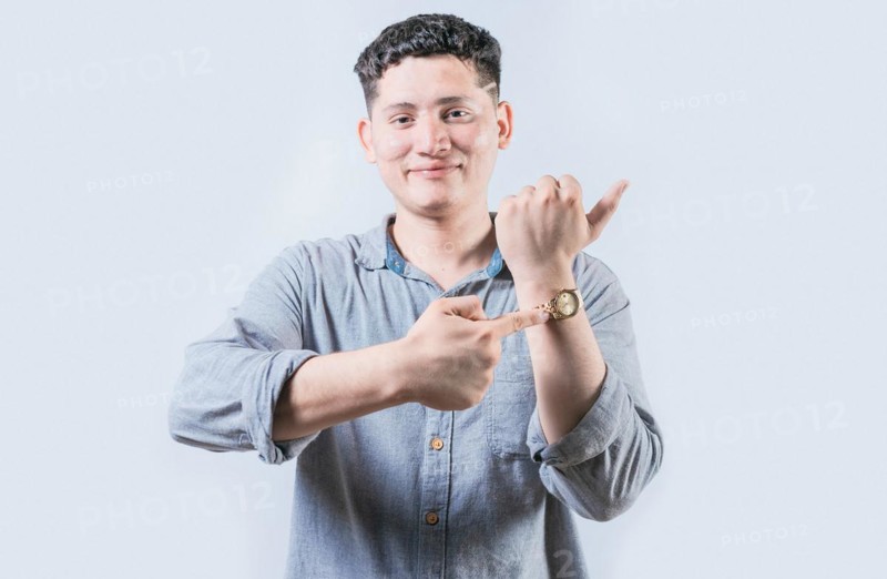 Smiling young man pointing at his wrist watch isolated. Portrait of person pointing his wrist watch on isolated background