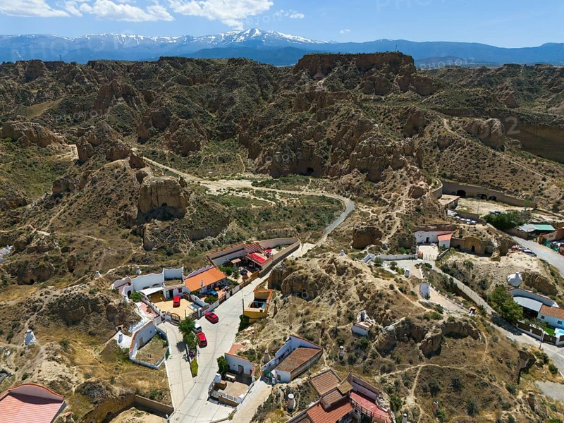 Mountain village with scattered houses and rocky landscape in the foreground, in a sunny valley with clear sky and mountains in the background, aerial view, cave dwellings, cave neighbourhood, Troglodytos, Guadix, Granada, Andalusia, Spain, Europe