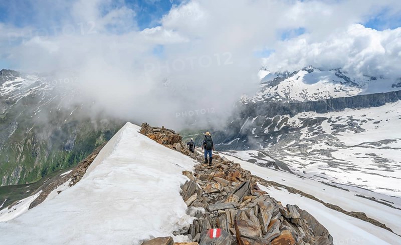 Mountaineer on a rocky ridge with snow, descent from the summit of Schönbichler Horn, view of snow-covered mountain peaks and valley Zemmgrund, Berliner Höhenweg, Zillertal Alps, Tyrol, Austria, Europe
