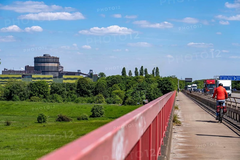 The ThyssenKrupp Steel steelworks in Duisburg-Beeckerwerth, blast furnaces 8 and 9 on the right, cyclist on the cycle path of the Beeckerwerth motorway bridge, A42, green Rhine meadows landscape, North Rhine-Westphalia, Germany, Europe
