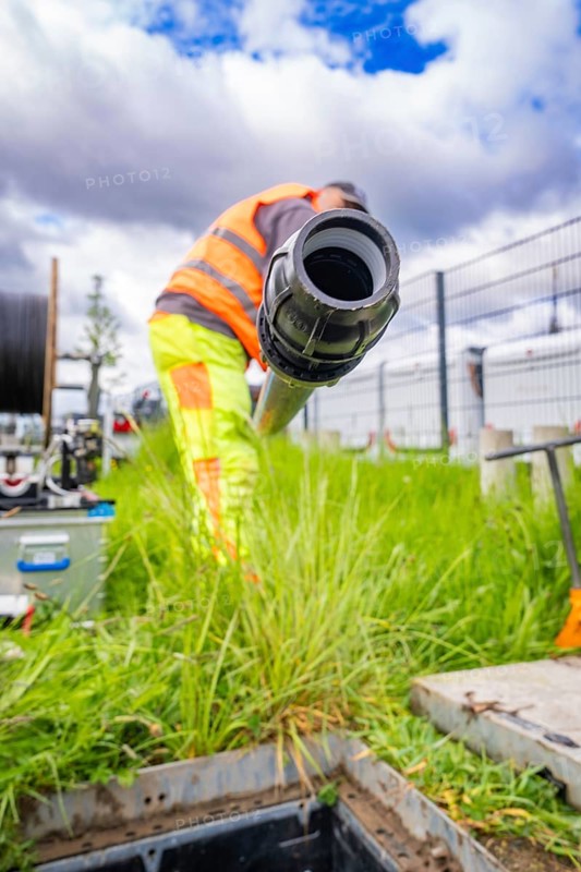 Worker in protective clothing holding a pipe and working in a meadow under a cloudy sky, construction fences in the background, fibre optic installation, Calw district, Black Forest, Germany, Europe