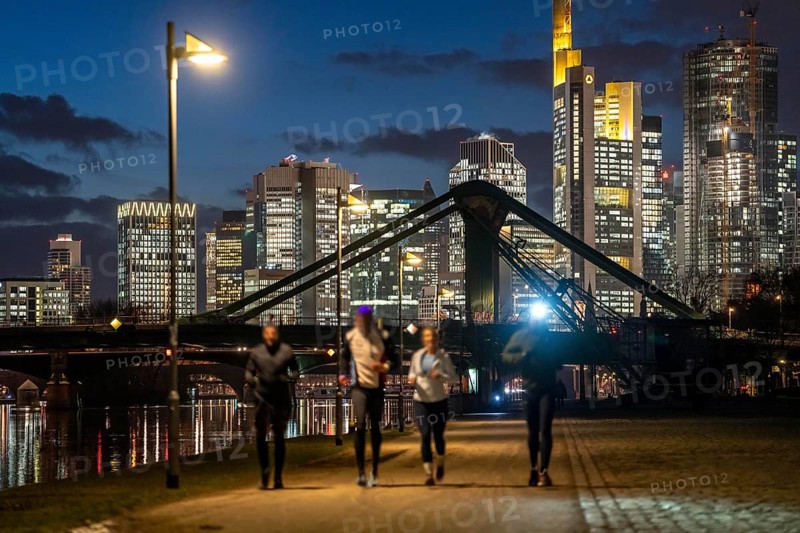 Skyline of the city centre of Frankfurt am Main, joggers on the pavement, promenade along the river Main, dusk, Hesse, Germany raft bridge in the background