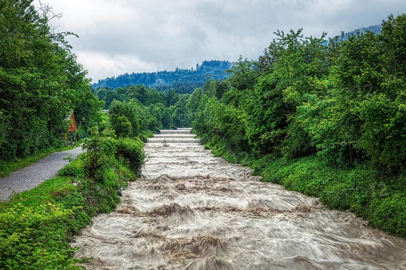 A river with a strong flow of water along a green landscape with wooded hills, Jenbach, Bad Feilnbach