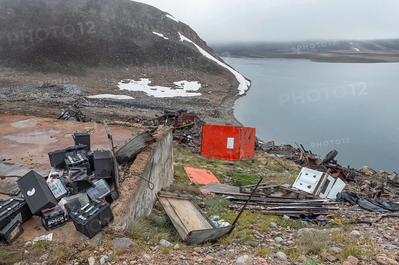 Old batteries, junkyard in rocky coastal landscape with snow remains, arctic settlement Ittoqqortoormiit, Scoresbysund or Scoresby Sund or Greenlandic Kangertittivaq, East Greenland, Greenland, North America