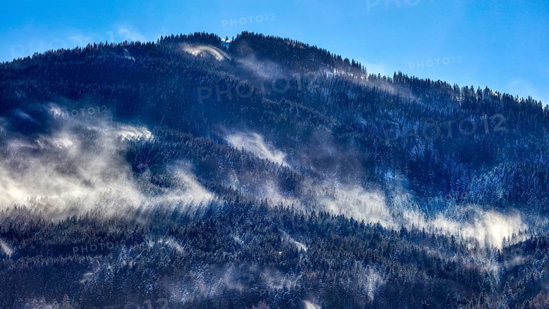 Misty mountains with snow and dense forests under a blue sky, Bad Feilnbach