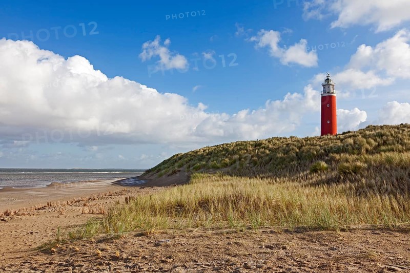 A red lighthouse stands on a grassy dune on the beach under a blue sky with clouds, Eierland lighthouse, Texel island, Netherlands