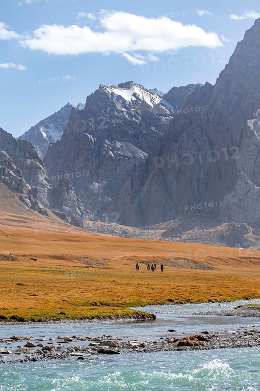 Rider in mountain landscape with yellow meadows, river Kol Suu and mountain peaks with glacier, Keltan Mountains, Sary Beles Mountains, Tien Shan, Naryn Province, Kyrgyzstan, Asia