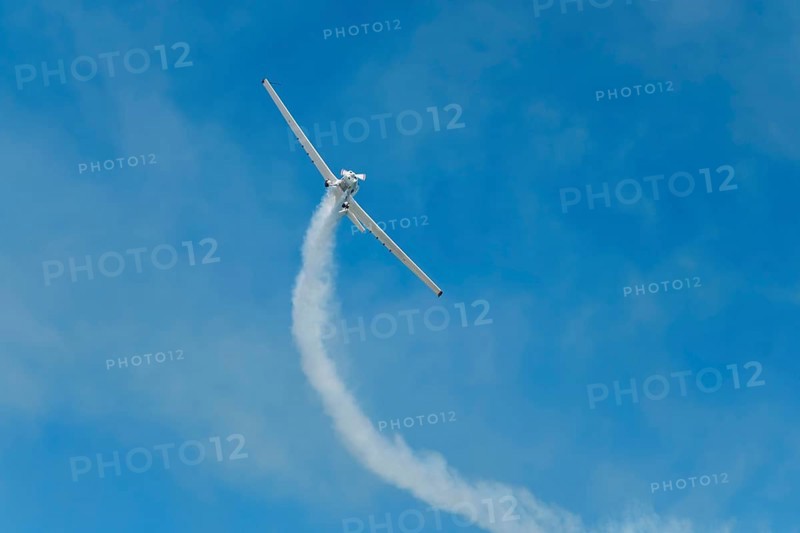Stunt aerobatic plane performing stunts in blue sky with smoke trail. Concept of teamwork, collaboration, coordination, trust, precision, difficulty, challenge, speed, synergy