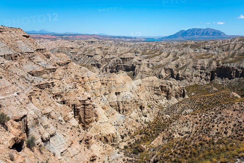 Large canyon area with rock formations and bare vegetation under a bright blue sky, Barranco de la Rambla del Pollo, Gorafe desert, Granada, Andalusia, Spain, Europe