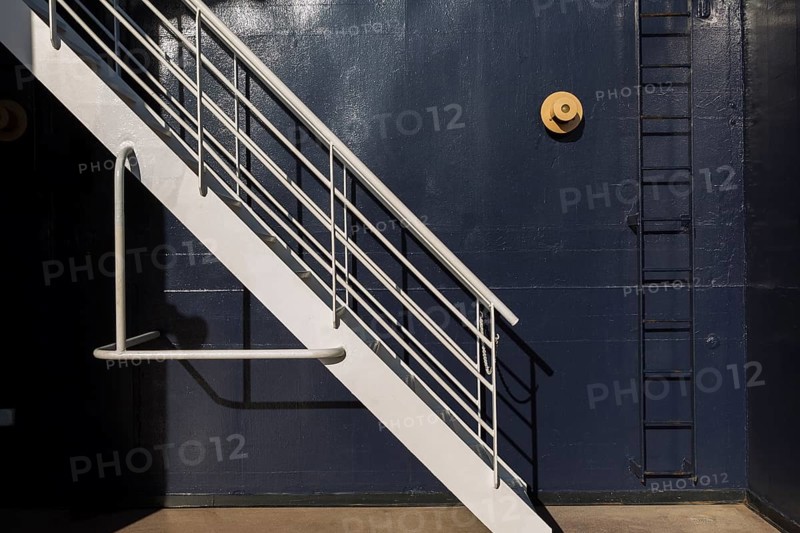 White painted metal stairs and black ladder against blue metal wall on a cruise ship, La Spezia, Italy, Europe