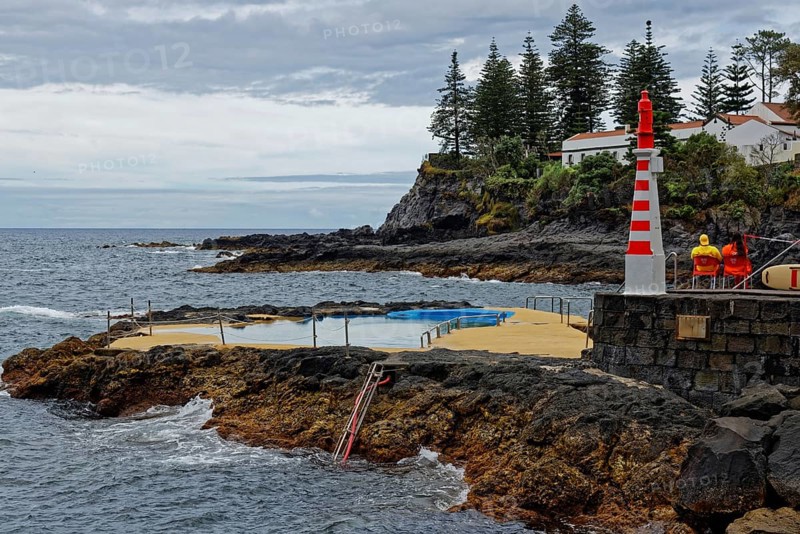 Small lighthouse and seawater swimming pool on the rocky coast under a cloudy sky, Caloura fishing village, Ribeira Chã, Sao Miguel Island, Azores, Portugal, Europe