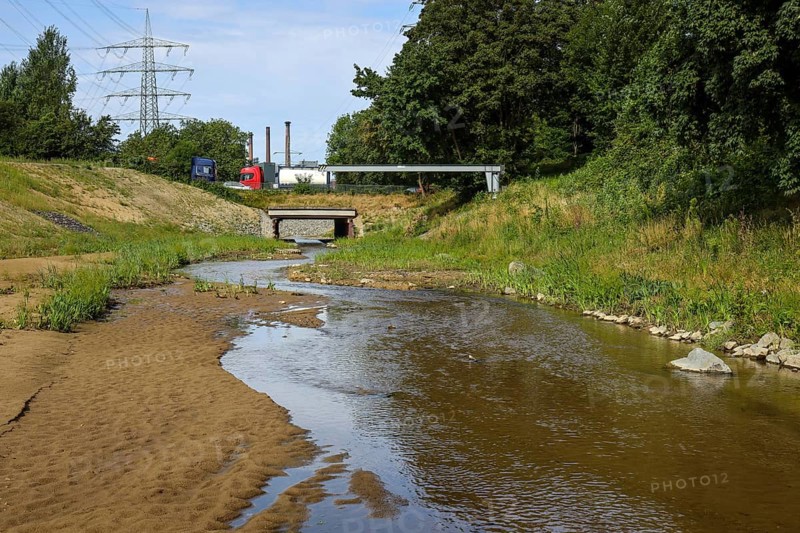 Bottrop, North Rhine-Westphalia, Germany, Renaturalised Boye, the tributary of the Emscher, was transformed into a near-natural watercourse, flood protection through newly designed flooding areas, the Boye is now free of wastewater after the construction of a parallel sewer, is part of the Emscher river system and thus part of the Emscher conversion, was previously an open, above-ground wastewater canal, mixed water canal with surface water and wastewater. At the back, car traffic on the B224 federal road bridge in front of the Prosper coking plant, ArcelorMittal Bottrop, Europe