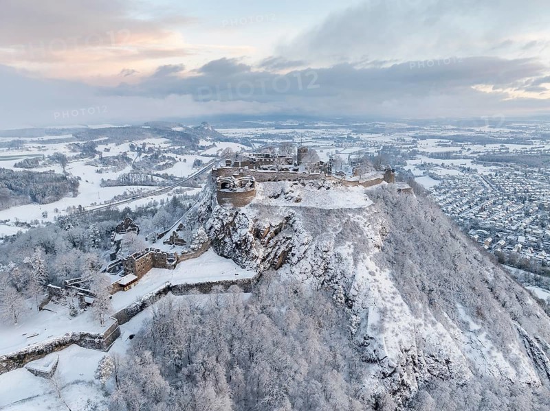 Aerial view of the snow-covered Hegau volcano Hohentwiel with Germany's largest castle ruin on a cold winter morning, in front of sunrise, surrounded by frosty trees in a winter landscape, on the horizon the neighbouring Hegau volcano Hohenkrähen, district of Constance, Baden-Württemberg, Germany, Europe