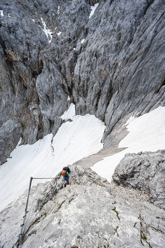 Mountaineer with helmet in a secured via ferrata, Zugspitze via ferrata, ascent to the Zugspitze, view of mountain basin with snow field of the Höllentalferner and Höllental, Wetterstein range, Bavaria, Germany, Europe