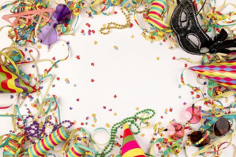 Colourful carnival paraphernalia such as hats, masks and confetti on a white background