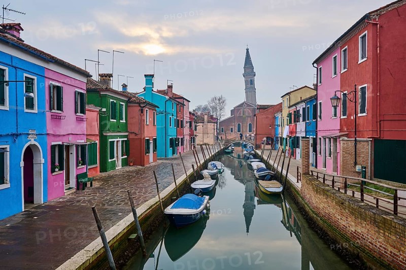 Colorful houses beside the waterway in between 'Riva dei Santi' and 'Fondamenta di Terranova' with boats lying in the water and church 'Chiesa Parrocchiale di San Martino Vescovo' in the background on the island of Burano, Italy, Europe