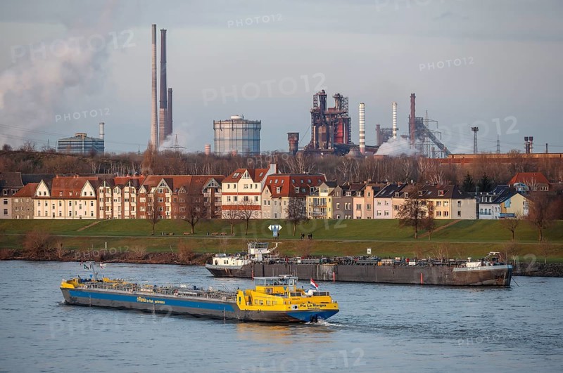 Duisburg, North Rhine-Westphalia, Germany - Cityscape in the Ruhr area with cargo ship on the Rhine in front of residential buildings in the Laar district and behind the blast furnace 8 of the ThyssenKrupp steelworks in Bruckhausen