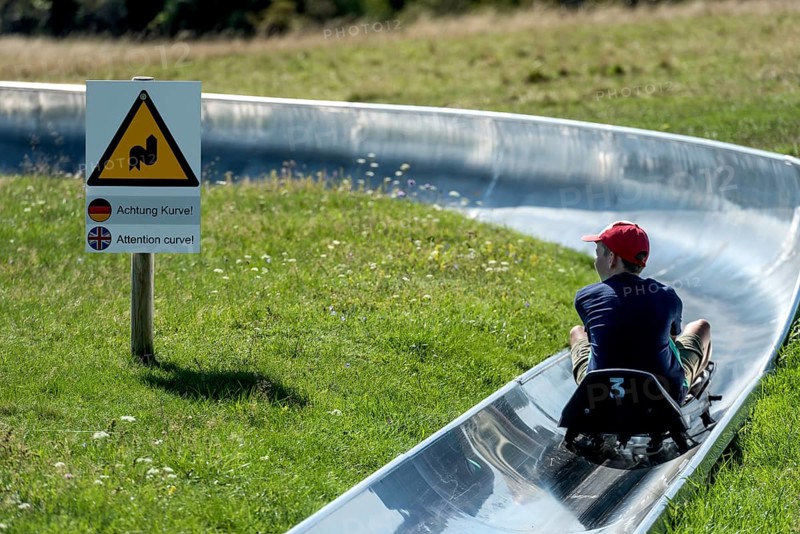 Boy with toboggan on the summer toboggan run, warning sign Attention curve, ski and toboggan arena, Hoherodskopf mountain summit, excursion destination, Schotten, Vogelsberg Volcanic Region nature park Park, Hesse, Germany, Europe