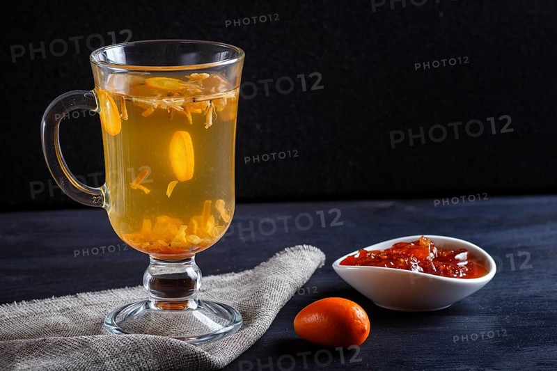 Jasmine tea with kumquat in a glass cup on a wooden board on a black background. close up, copy space