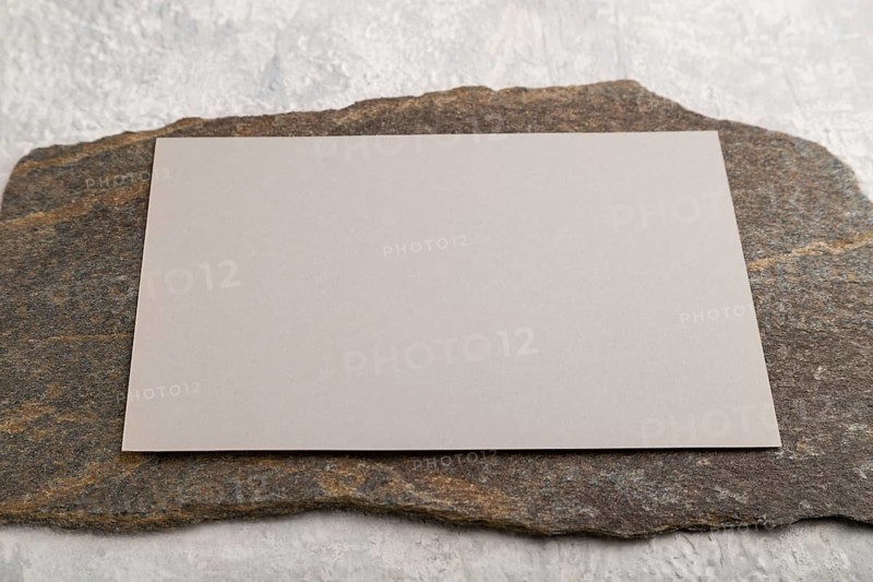Beige paper business card, mockup with natural stone on gray concrete background. Blank, side view, still life, copy space