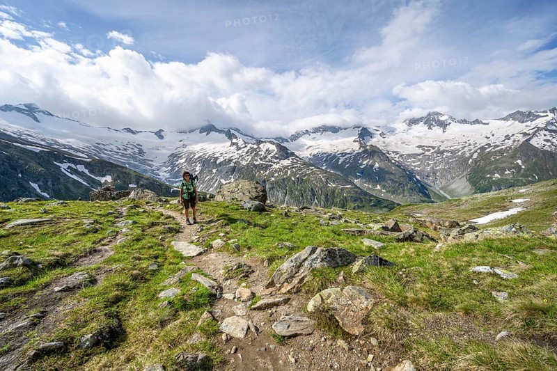 Mountaineer on hiking trail in picturesque mountain landscape, mountain peak with snow and glacier Schwarzensteinkees, Hornkees and Waxeggkees, summit Schwarzenstein, Hornspitzen and Großer Möseler, Berliner Höhenweg, Zillertal Alps, Tyrol, Austria, Europe