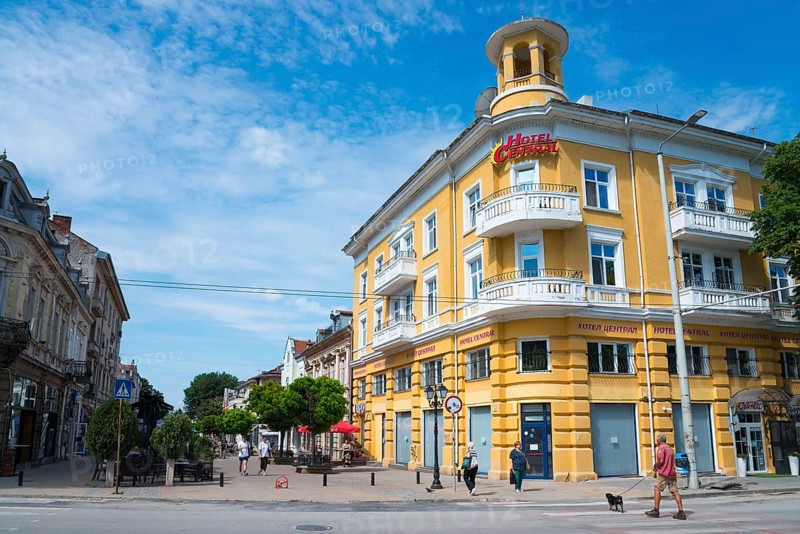 A yellow hotel building under a light blue sky with few clouds and passers-by on the street, hotel in the pedestrian zone Alexandrovska, Russe, Rousse, Ruse, Pyce, Bulgaria, Europe