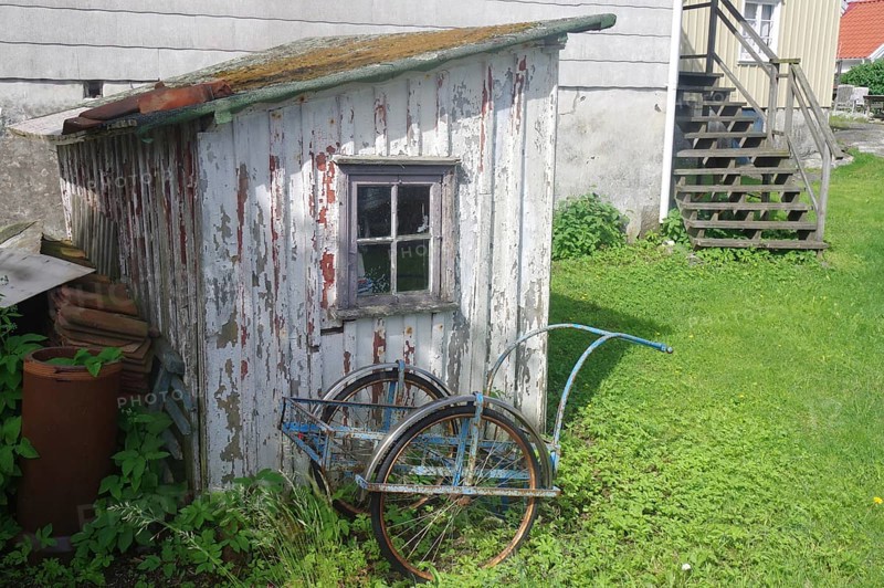 An old, weathered wooden shed with a bicycle trailer in front of it, surrounded by grass and a rural ambience, means of transport on a car-free island, Gullholmen, Orust, Sweden, Europe
