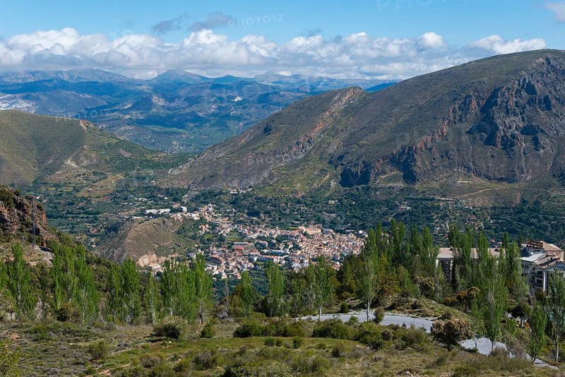View over a valley with a village surrounded by mountains, lots of greenery and a cloudy sky, mountain village Güéjar Sierra, Güejar, Granada province, Andalucia, Spain, Europe