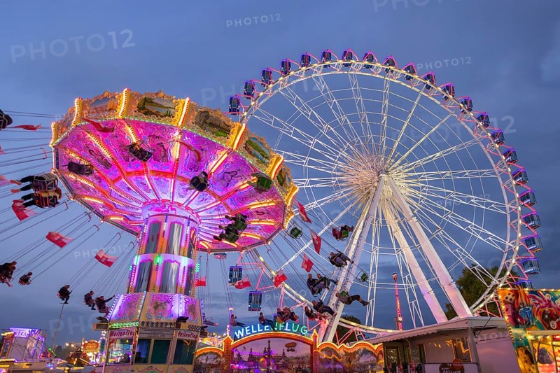 A lively funfair at dusk, illuminated by a large Ferris wheel and a colourful chain carousel, Cannstadter Volksfest, Stuttgart-Bad Cannstadt, Baden-Württemberg