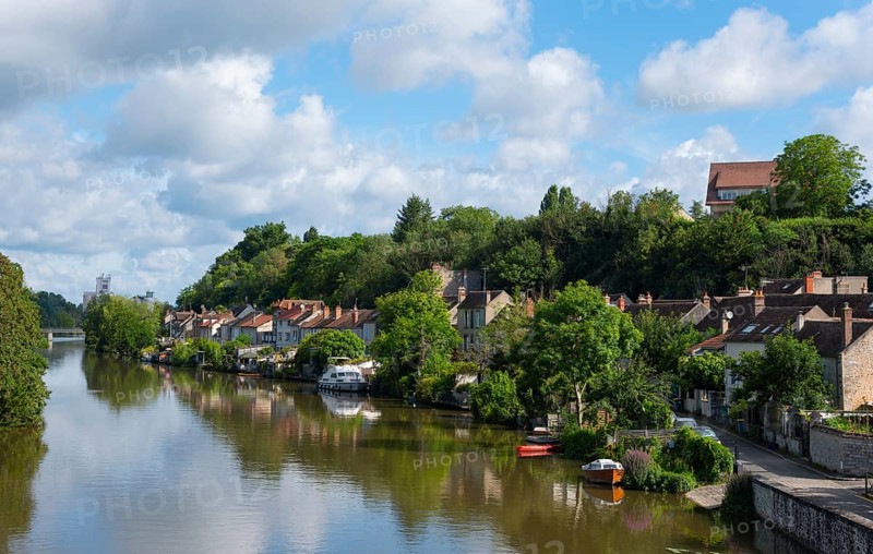 Flusslandschaft mit Uferhäusern und üppigem Grün unter einem teilweise bewölkten Himmel, Nemours am Fluss Loing, Département Seine-et-Marne, Region Île-de-France, Ile-de-France, Frankreich