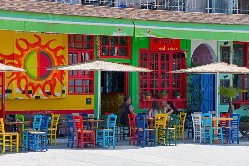 A lively street bar with colourful chairs and a colourful façade, guests under parasols, Sarti, Sithonia, Halkidiki, Halkidiki, Central Macedonia, Greece, Europe