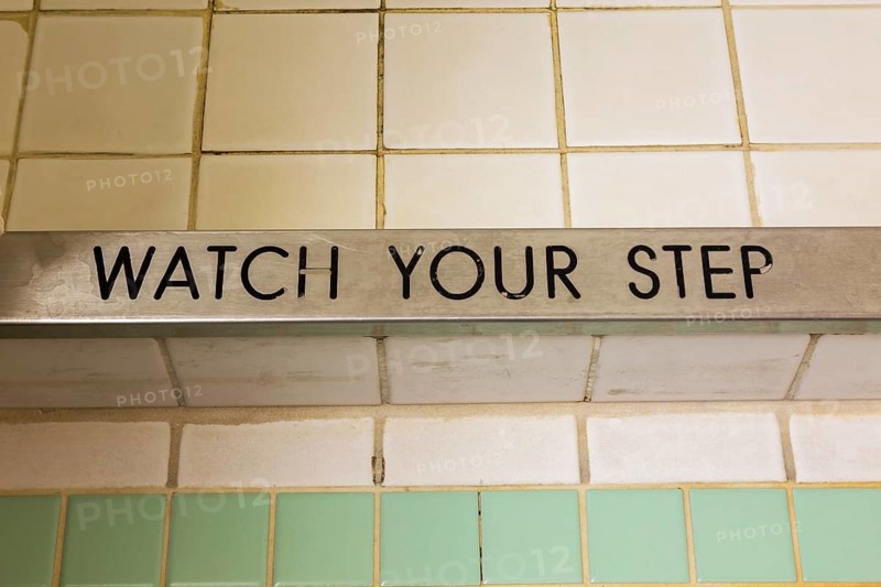 Top view of engraved Watch Your Step black lettering on chrome steel step of shower stall with ceramic tile floor, La Spezia, Italy, Europe