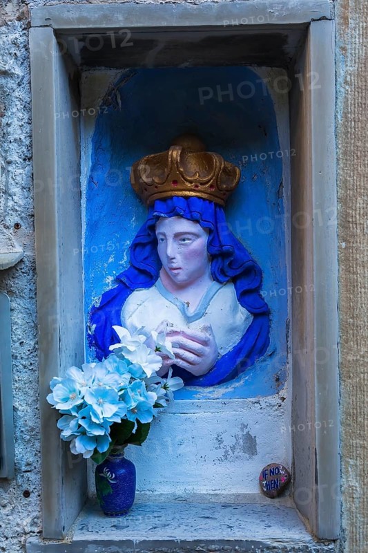 Religious blue and white with golden crown female with praying hands sculpture and silk flowers in ceramic vase in recess in stone wall, Manarola, Cinque Terre, La Spezia province, Italy, Europe