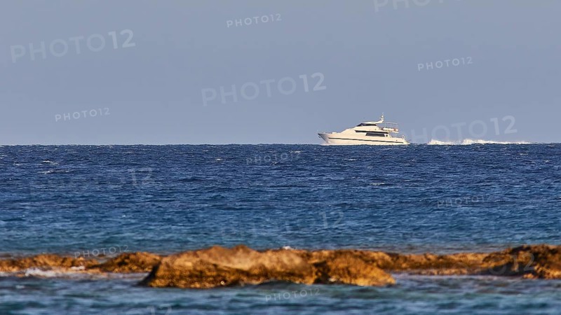 Luxury yacht sailing on the horizon over the blue sea with rocky coast, windsurfer, Meltemi windsurfing area, Devils Bay, Paralia Vatha, Vatha Beach, southeast coast, Karpathos, Dodecanese, Greek Islands, Greece, Europe