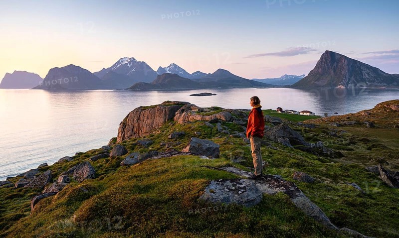 Landscape at Stornappstinden mountain. A hiker looks out over the landscape. View of the mountains Hogskolmen, Himmeltindan, Veggen and Mannen near Haukland, on the right Offersoykammen, all Vestvagoya. At night at the time of the midnight sun in good weather. Early summer. Flakstadoya, Lofoten, Norway, Europe