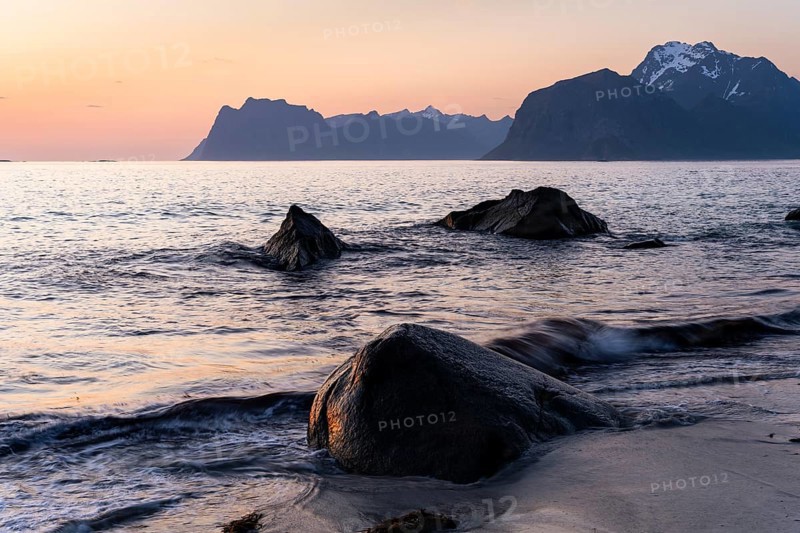 Seascape. On the beach at Myrland. Rocks and sea, with Mount Hogskolmen in the background on the left, Mount Veggen and Mount Mannen on the right and the snow-covered Himmeltindan behind. At night at the time of the midnight sun in good weather. Early summer. Lofoten, Norway, Europe