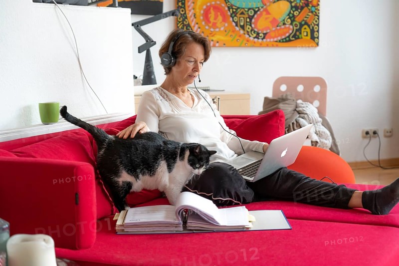 Woman, mid-50s, works from home, with laptop and communicates with colleagues via headset, home office, on the sofa
