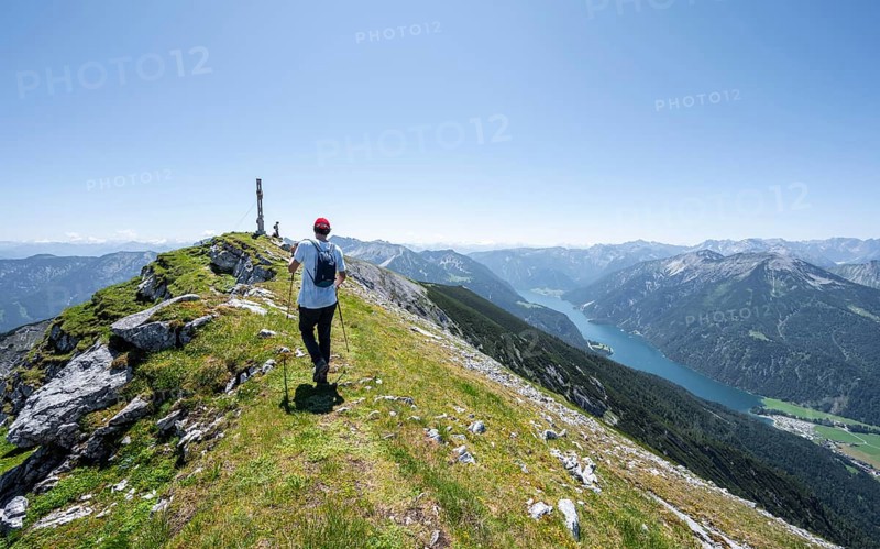 Mountaineer at the summit of Hochunnütz with summit cross, behind Achensee and summit of Seekarspitze, Unnütz crossing, Brandenberg Alps, Tyrol, Austria, Europe