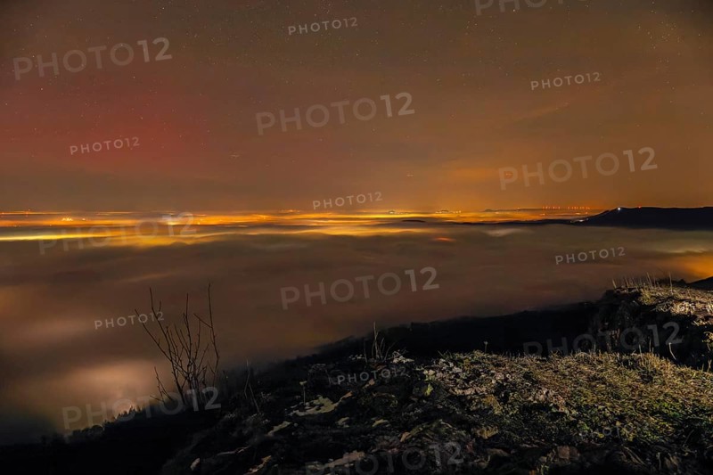 Firework lights under the sea of fog. New Year's Eve fireworks 2024 and a little red Aurora Borealis Northern Lights. On the Breitenstein, Swabian Alb near Ochsenwang. Sea of fog in the foothills of the Alb. View of the Drei Kaiserberge near Göppingen. In the foreground the Aichelberg with the Bossler