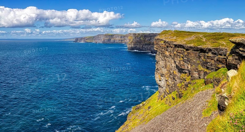 Sunlit cliffs on an endless blue coastline under a clear sky, Cliffs of Moher