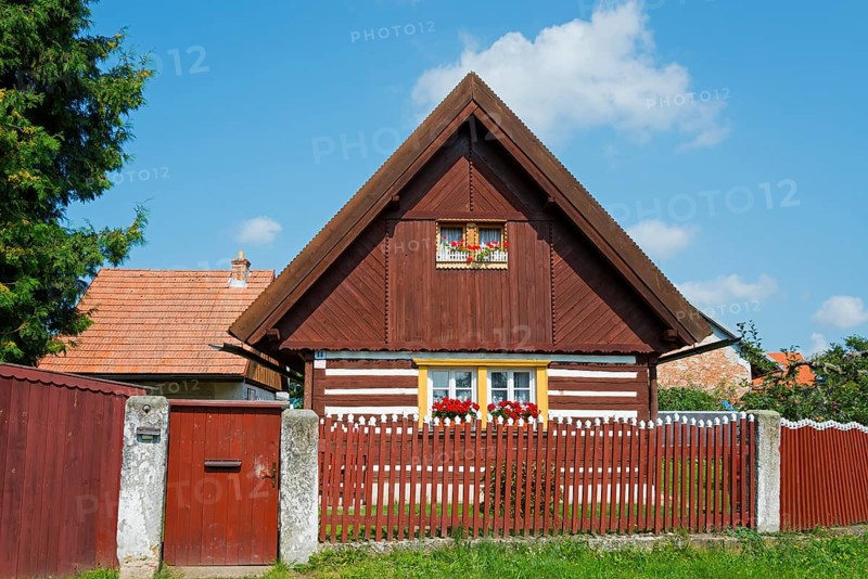 Brown wooden house with a gable and red shutters, surrounded by a wooden fence and flowers, Old wooden house, Vesec u Sobotky, village conservation area, Libošovice, Libosovice, Okres Jicín, Hradec Králové, Czech Republic, Europe
