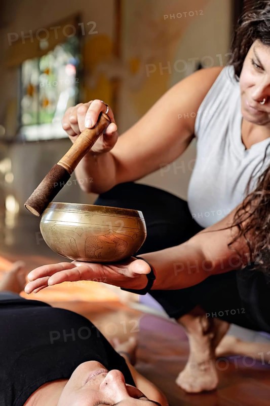 Latin yoga teacher with a singing bowl inducing relaxation at the end of yoga class. Vertical image, blurred background