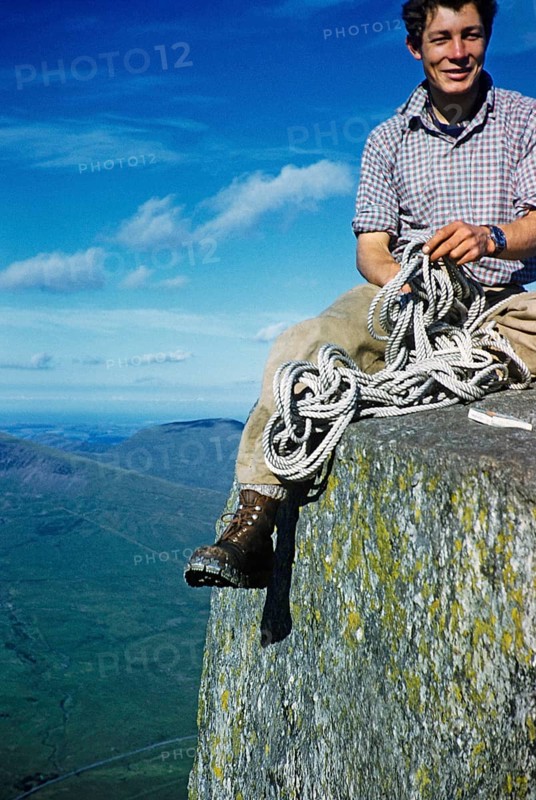 Young male climber sitting high up on a rock and holding a climbing rope, probably North Wales, Great Britain, around 1958