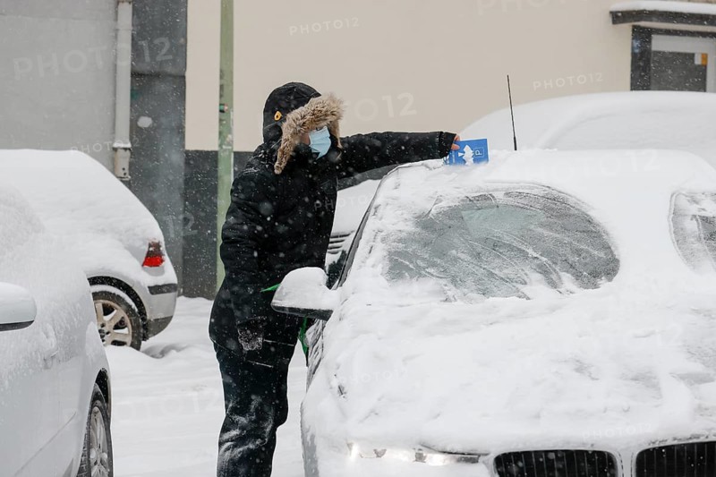 Essen, North Rhine-Westphalia, Germany - Onset of winter in the Ruhr area, driver with mask scrapes snow and ice off the car with a parking disc in times of the corona pandemic