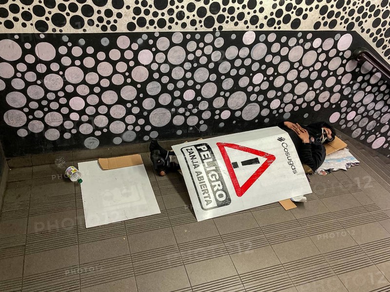 Homeless man sleeping in the entrance of the underground covered with a warning sign reading Danger, open ditch, Buenos Aires, Argentina, South America