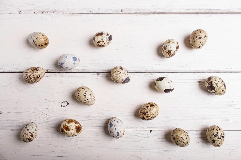 Raw quail eggs on a white wooden background, top view